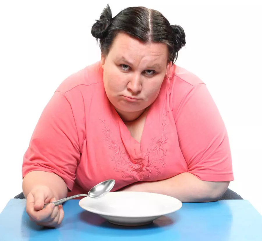 Женщина в весе грустит над пустой тарелкой