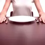 Девушка за столом с пустой тарелкой и приборами