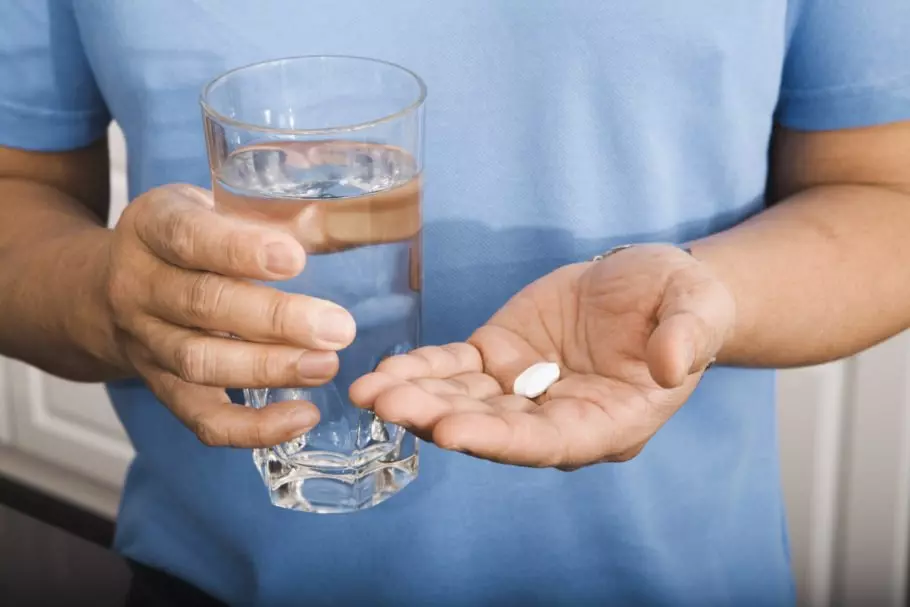 в руках мужчины стакан с водой и таблетки